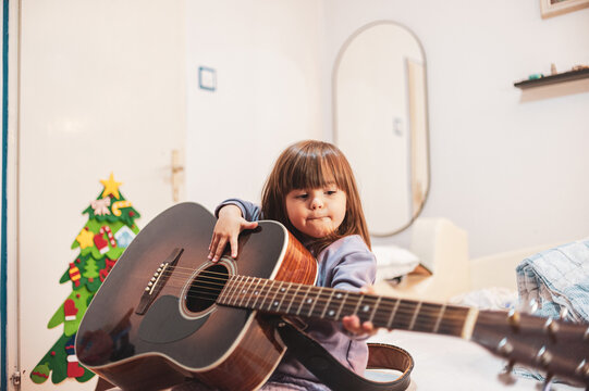 A little girl is learning to play an acoustic guitar	