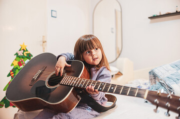 A little girl is learning to play an acoustic guitar 