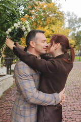 Romantic couple embracing closely and sharing a tender kiss, holding a bouquet of white flowers on a cobblestone path in autumn