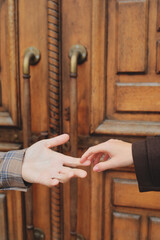 Close-up of a couple's hands reaching out to touch, symbolizing connection and affection against a massive old wooden door