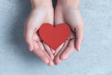 Obraz premium Hands holding red paper heart symbol of love and care on gray background, expressing warmth and affection