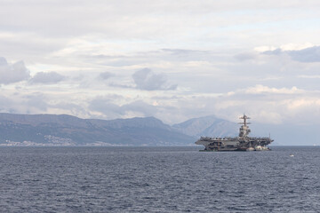Aircraft Carrier on Open Sea Near Distant Mountain Range Under a Cloudy Sky