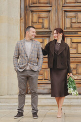 Elegant couple posing and showing affection on stone steps in front of a massive ornate wooden door of a historic building
