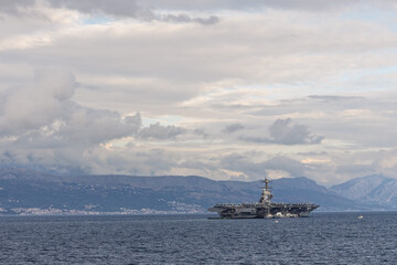 Aircraft Carrier on Open Sea Near Distant Mountain Range Under a Cloudy Sky
