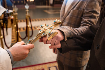 Close-up of hands receiving an ornate golden crucifix with turquoise stones from a priest during a traditional orthodox church ceremony