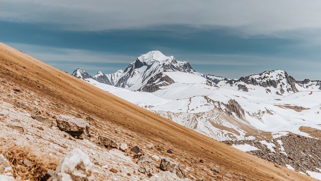 Snow-covered mountain range with a sloped, rocky foreground and a clear sky.