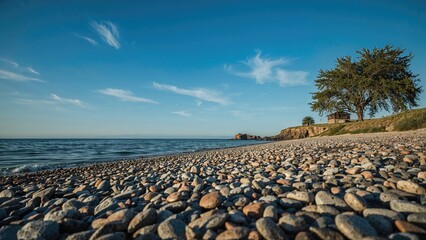 A scenic coastal landscape with rocks on the shore, calm sea, and trees under a blue sky with clouds.