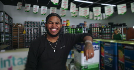 Smiling store clerk leaning on stacked paint cans in a hardware store, showcasing customer-friendly service in a vibrant, product-filled workspace