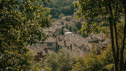 A quaint village with tiled rooftops nestled among lush green trees and hills.