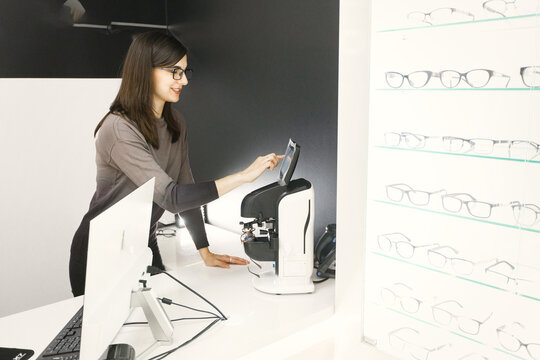Professional female optician checking eyeglasses in special machine