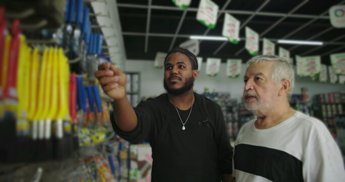 Store clerk explaining product options to a customer in a hardware store aisle, highlighting attentive service and showcasing available tools and paint supplies
