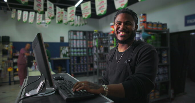 One Smiling Black store clerk interacting with customers, computer on desk in a well-organized retail shop, positive customer service and approachable demeanor
