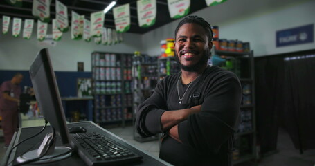 One Black male retail employee with arms crossed, confidently standing at counter, shop interior visible, engaging and professional customer service approach
