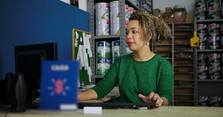 Young woman using a computer at a desk in a hardware store, focused and smiling, engaging in professional work in a retail business environment