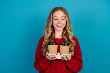 Adorable young woman in red sweater holding coffee cups against vibrant blue backdrop in cheerful casual style