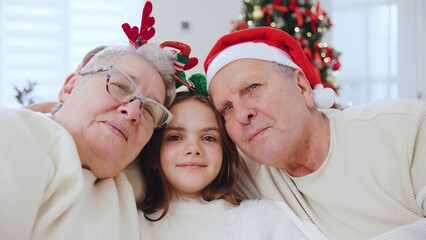 Portrait of Elderly couple celebrates New Year with their granddaughter, sharing joy and warmth by the Christmas tree in a cozy home setting