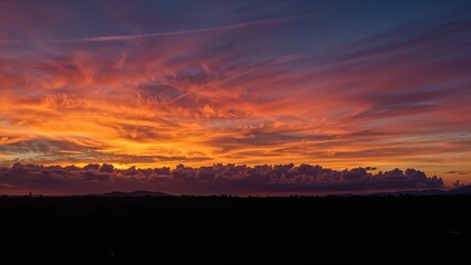 Fototapeta premium Vivid sunset sky with orange, pink, and purple hues over a dark landscape.