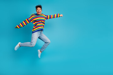 Obraz premium Joyful young woman jumps in striped sweater light jeans against a bold blue background for lifestyle fashion and advertising use