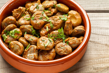 Clay tapas bowl with vegan version of Spanish habas con jamón. Broad beans with second skin cooked in white wine and olive oil  with garlic, onion, and smoked paprika.