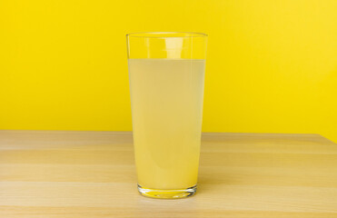 A glass of lemon juice on a table with a yellow background. Lemon juice. Yellow liquid in a glass.