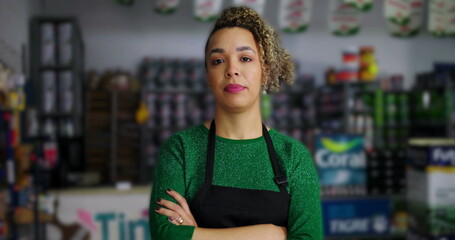 Professional female business owner in hardware store, arms crossed, standing among tools and paint supplies, representing independence and success in retail