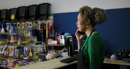 Obraz premium Dedicated shopkeeper on a phone call at the counter in a hardware store, surrounded by tools and supplies, managing tasks with professionalism and focus