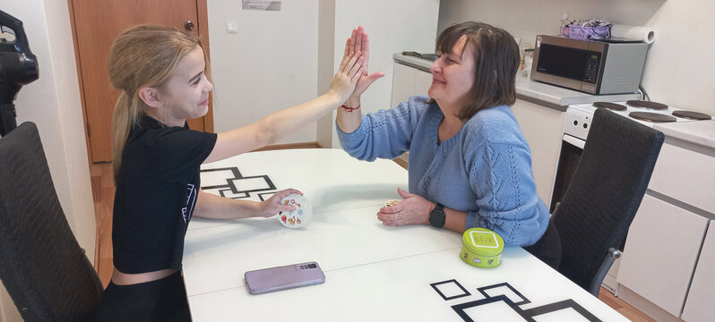 A young girl and an older woman high-five each other at the kitchen table.