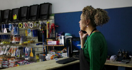 Obraz premium Dedicated shopkeeper on a phone call at the counter in a hardware store, surrounded by tools and supplies, managing tasks with professionalism and focus