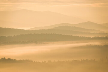 SILHOUETTE: Morning mist gently spreads over mountain valleys and forests, with ridges peeking out. Layered hills fade into distance, creating a calm and dreamy winter atmosphere bathed in soft light.