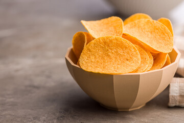 Crispy potato chips in bowl on kitchen table.