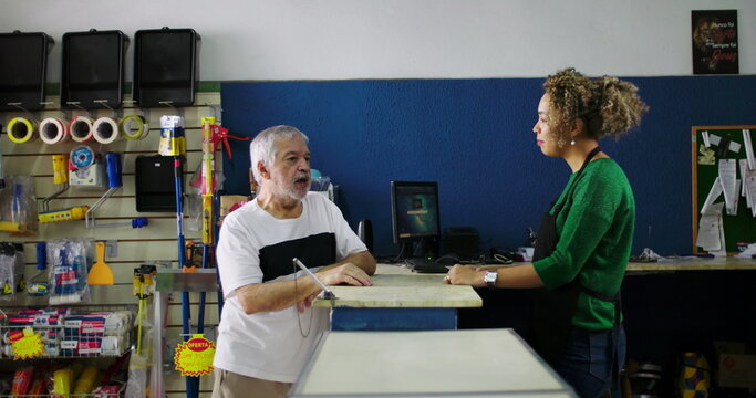 Shopkeeper attentively listening to an elderly customer at the counter in a hardware store, demonstrating patience and understanding in customer interaction