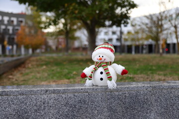 Snowman toy in a warm city, Christmas decoration in urban background, winter in warm country