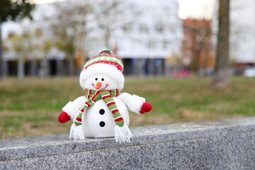 Snowman toy in a warm city, Christmas decoration in urban background, winter in warm country