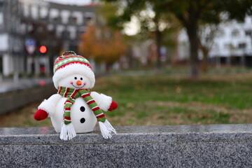 Snowman toy in a warm city, Christmas decoration in urban background, winter in warm country