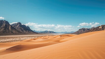 Desert landscape with sand dunes, mountains, and blue sky.