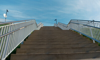 Naklejka premium Upward perspective of outdoor staircase with white metal railings against blue sky (this image was made with an anamorphic lens)