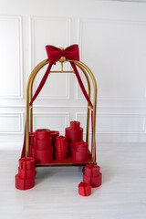 Elegant hotel luggage cart decorated with a big red bow and filled with red gift boxes. Festive holiday or luxury celebration concept in bright, minimal interior