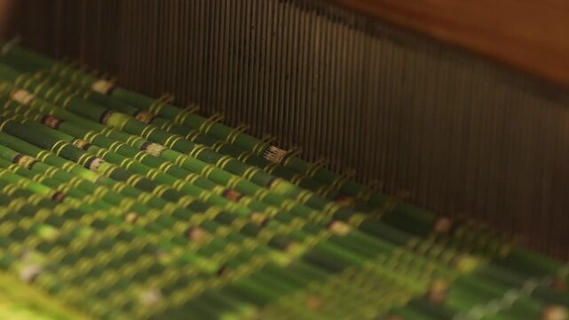 Detailed view of a weaving process using green plant stalks and thin threads on a wooden loom. A hand gently guides the material through the pattern.