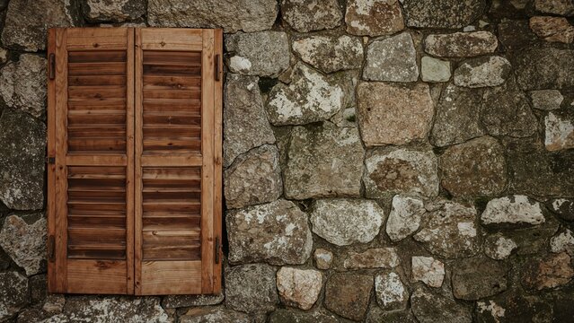 A wooden window shutter mounted on an old stone wall.