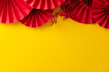 Red paper fans and plum blossom branches creating an upper border on a yellow background with copy space below.