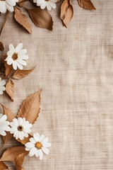 A vertical rustic composition featuring dried brown leaves and white flowers arranged on a textured beige fabric background with ample copy space for autumn greetings and nature designs.