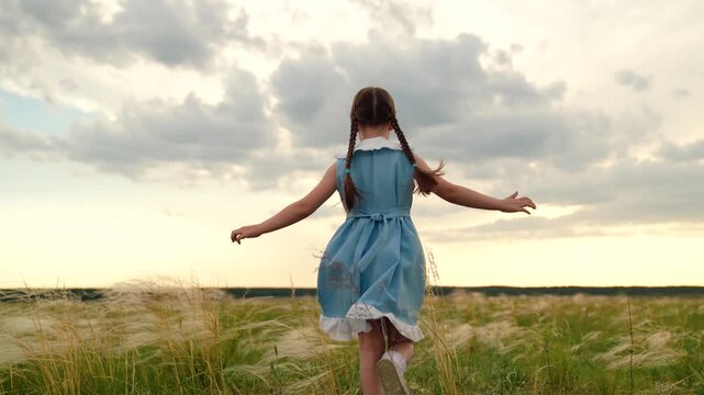 Baby girl playing superhero in nature. kid girl run in park. Happy little girl in dress running with raised hands on grass meadow. Children's dreams. Cheerful little girl play running in summer park