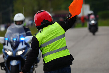 traffic marshal in a fluorescent safety vest flagging beside the police motorcycle during the race