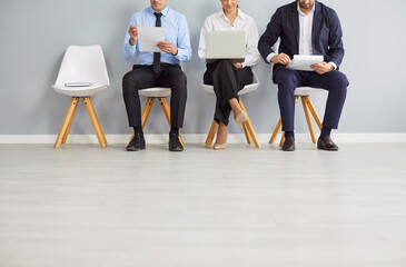 A group of business people are sitting on chairs in a row against the wall, close-up. Candidates...