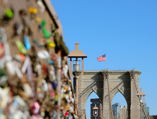 ribbons and wires and bows tied to the brooklyn bridge in new york city as a memorial for victims and the usa flag on the tower in the background