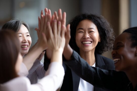 Diverse women, including Asian and African American, display teamwork, giving high five, smiling cheerfully.