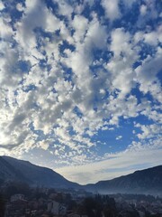 A valley city beneath dramatic morning altocumulus clouds illuminated by soft sunlight.