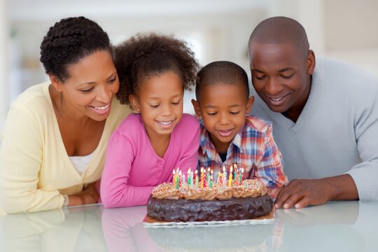 African American parents and children smiling, looking at chocolate birthday cake with many colorful candles.