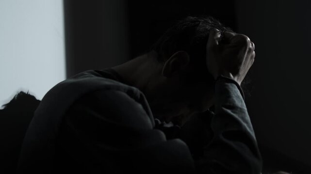 Man battling intrusive thoughts, holding head in darkness, mental struggle concept