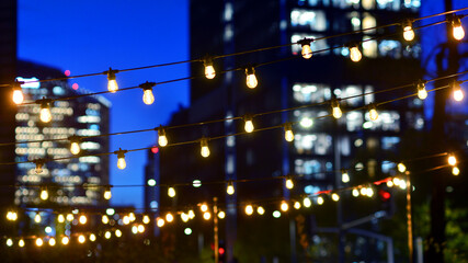 Light bulbs garlands against glass modern buildings background in night. Blurred rows of lit windows out the architectural grid of a modern facade.